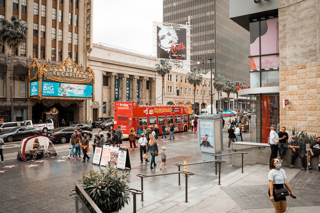 El Capitan Theatre, red double-decker bus, and city buildings in Hollywood, Los Angeles, highlighting iconic landmarks and urban activity with pedestrians amidst a bustling urban atmosphere.
