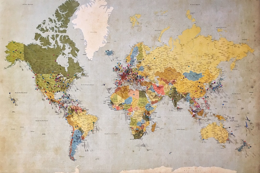 Vintage world map with colorful pins marking global destinations and travel routes across continents, set against a distressed background highlighting worldwide exploration.